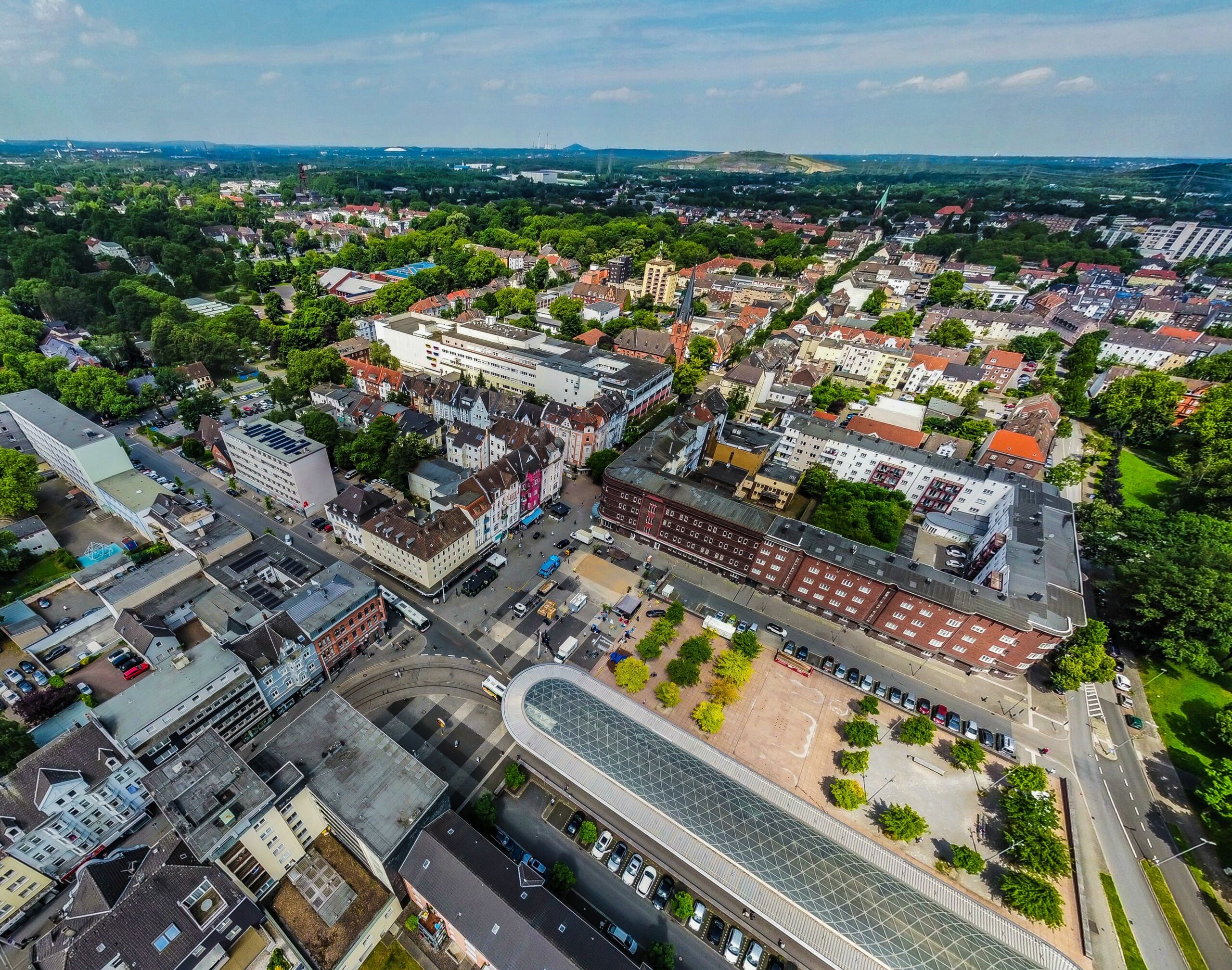 Drohnenaufnahme Wanne_MB Auf dem Foto ist eine Drohnenaufnahme von Wanne-Mitte zu sehen. In der Bildmitte ist die Hauptstraße zu sehen und der Buschmannshof, an den der Busbahnhof direkt angrenzt. Das avisierte Gebäude für das KUBIRUHR befindet sich auf der Ecke Buschmannshof / Hauptstraße.