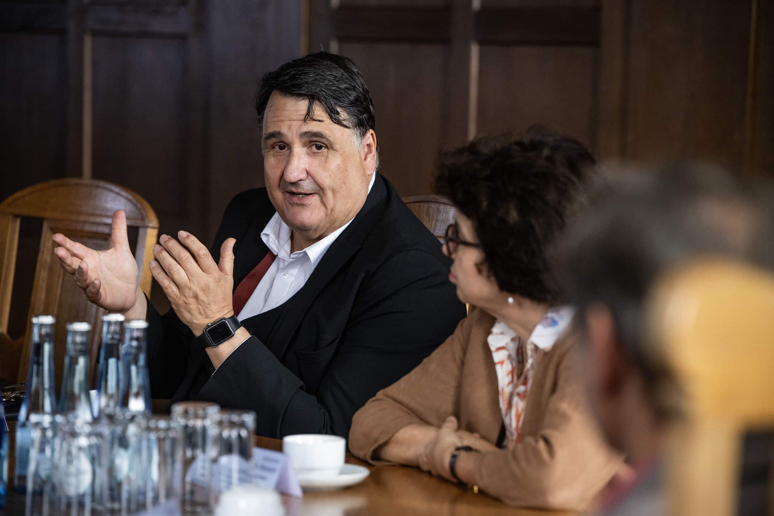 Personen reden an einem Tisch im Herner Rathaus. Im Fokus ist der Rektor der Ruhr-Universität Bochum, Prof. Dr. Dr. h. c. Martin Paul. Auf dem Tisch stehen diverse Getränke.